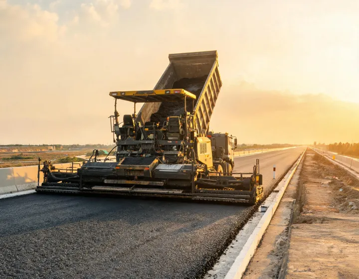 Asphalt paver screed laying binder course with material transfer vehicle ahead
