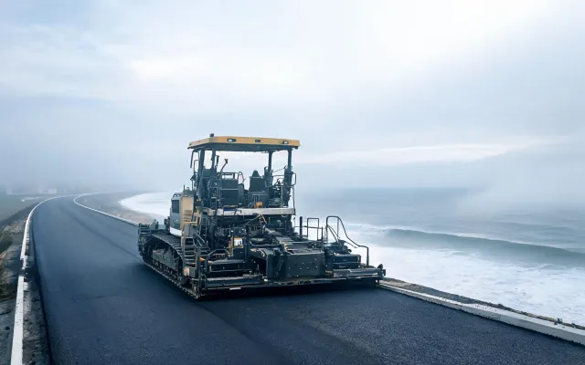Coastal highway asphalt overlay with paver near sea mist