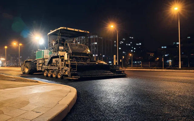 Urban night paving with wheeled paver under streetlights